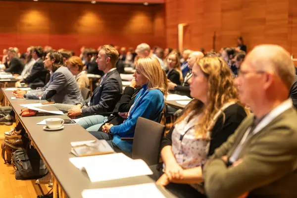 Mehrere Personen sitzen an einem langen Tisch und lauschen der Konferenz