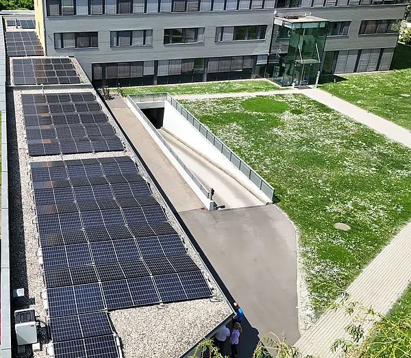 Nahaufnahme einer Luftaufnahme mit Solarpaneelen auf dem Dach eines Bürogebäudes, darunter ein Teil der grünen Wiese.