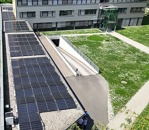 Nahaufnahme einer Luftaufnahme mit Solarpaneelen auf dem Dach eines Bürogebäudes, darunter ein Teil der grünen Wiese.
