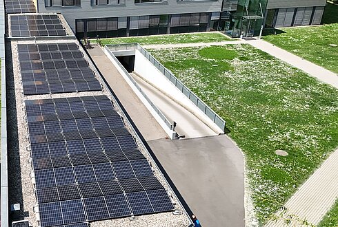 Nahaufnahme einer Luftaufnahme mit Solarpaneelen auf dem Dach eines Bürogebäudes, darunter ein Teil der grünen Wiese.