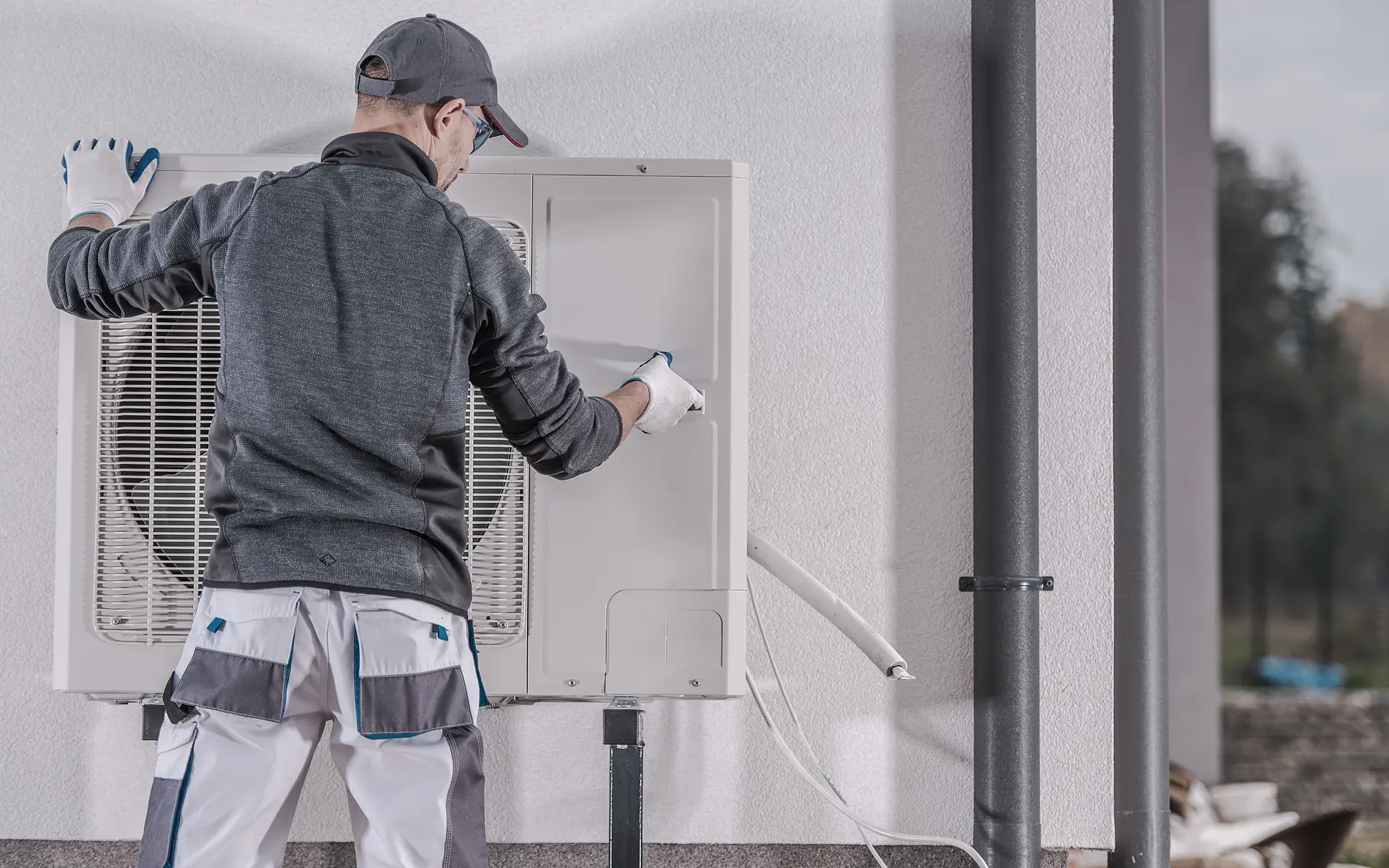 Ein Arbeiter steht vor einer Luftwärmepumpe und schraubt daran.