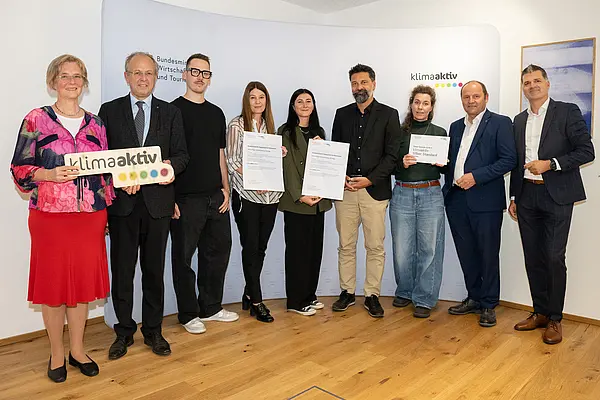 eine Gruppe von Menschen auf einer Bühne hält Urkunden in die Kamera
