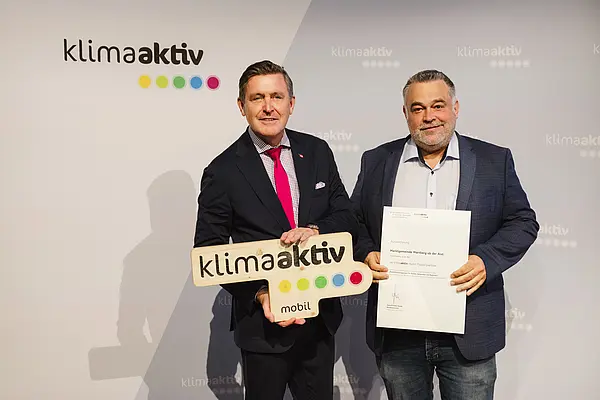 Menschen mit Urkunde und klimaaktiv Schild lächeln in die Kamera