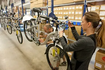 Mehrere Fahrräder wurden erhöht befestigt und berühren den Boden nicht. Zwei Personen sehen sich das Rad genauer an und tasten an Reifen und Lenkstange ab.