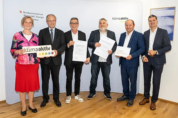 eine Gruppe von Menschen auf einer Bühne hält Urkunden in die Kamera