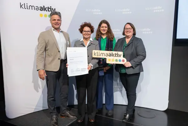 4 Personen mit Urkunde und klimaaktiv Schild schauen in die Kamera