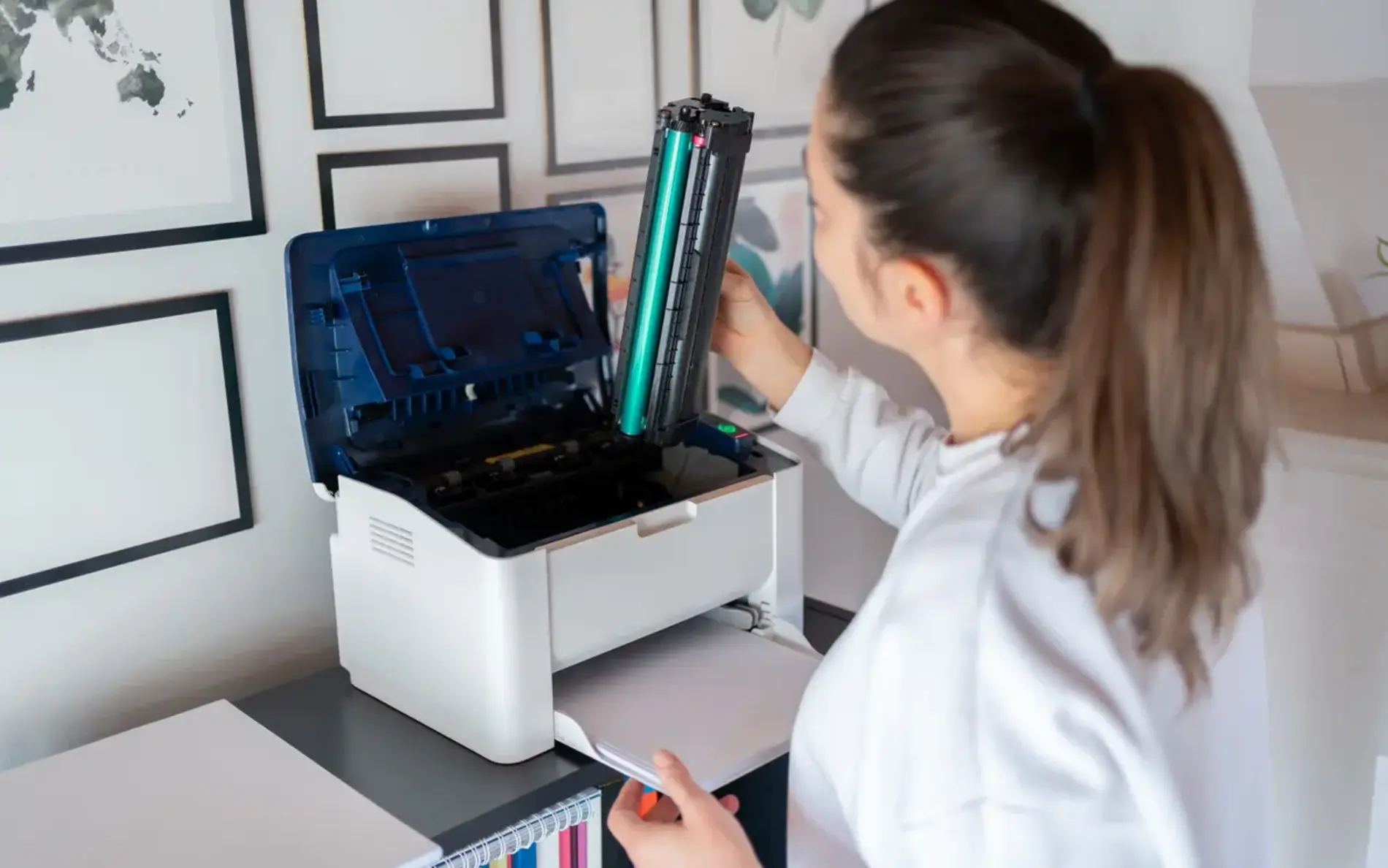 Eine Frau mit Pferdeschwanz steht vor einem Drucker und wechelt die Patrone.