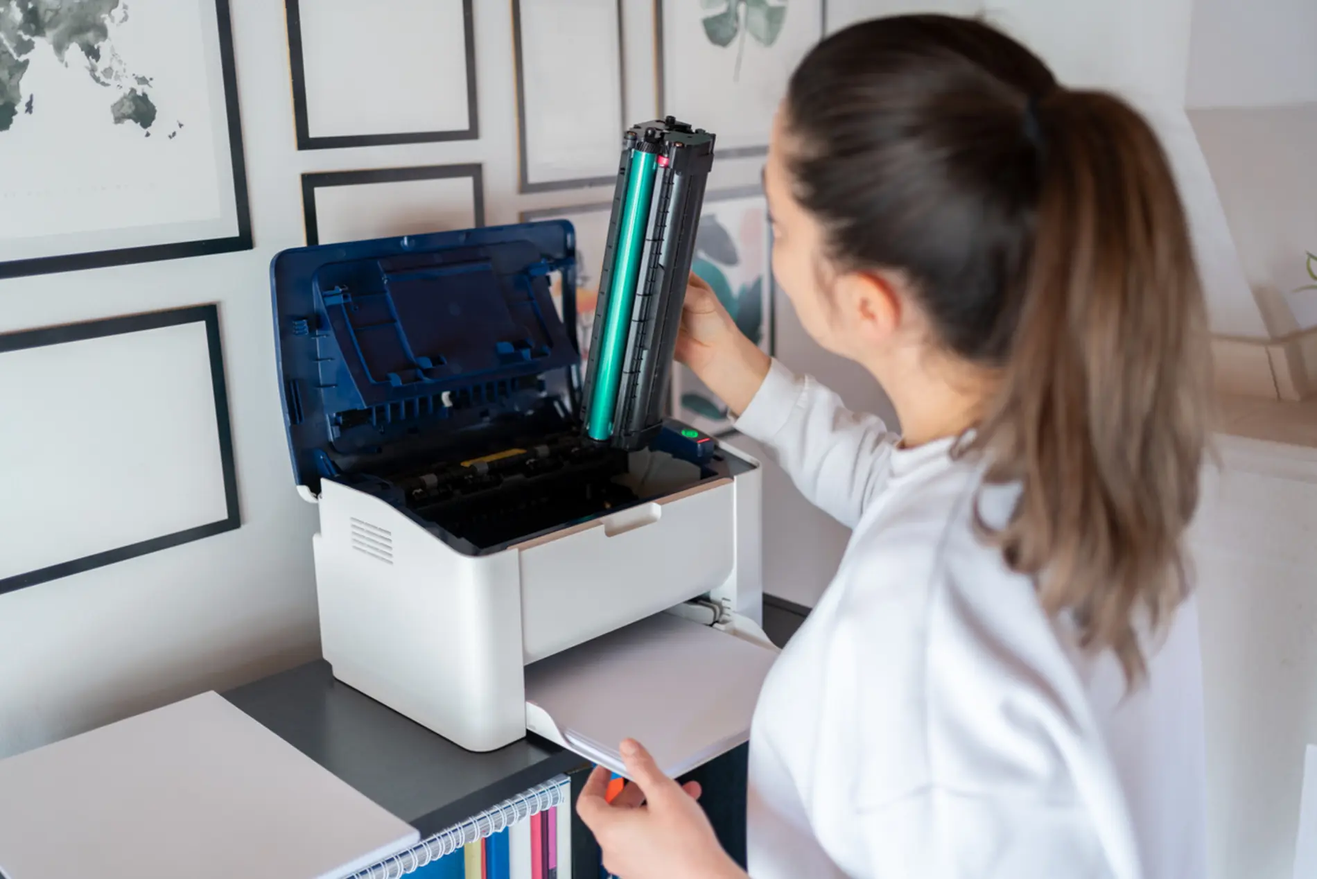 Eine Frau mit Pferdeschwanz steht vor einem Drucker und wechelt die Patrone.