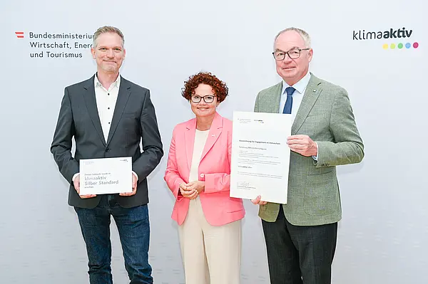 Personen mit Urkunde schauen in die Kamera