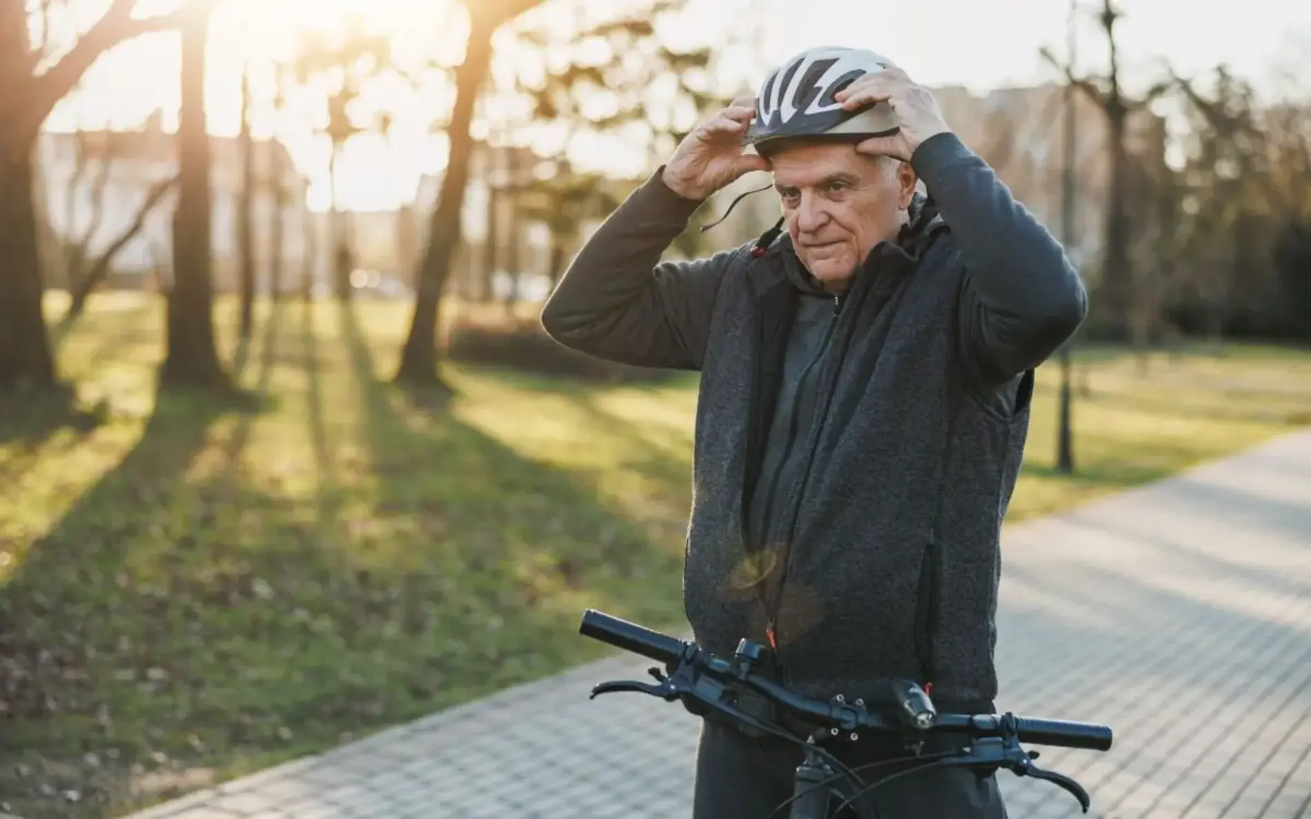 Ein älterer Mann mit steht mit dem Fahrrad auf einem Weg und setzt sich gerade den Fahrradhelm auf