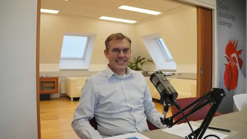 Fritz Hudribusch sitzt im Besprechungsraum der AEA vor dem Podcastmikrofon.