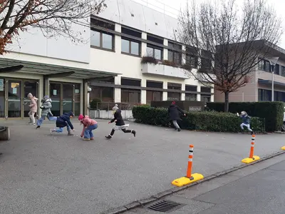 mobile Poller vor der Schule entlang zum Gehsteig. Kinder laufen über den Schulplatz im Hintergrund ein langes weißtes Schulgebäude