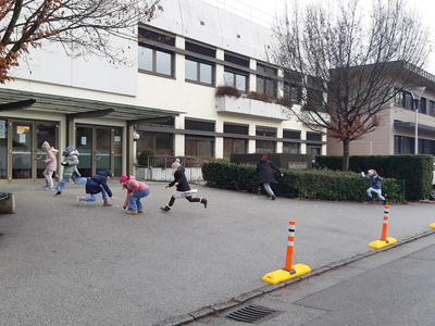 mobile Poller vor der Schule entlang zum Gehsteig. Kinder laufen über den Schulplatz im Hintergrund ein langes weißtes Schulgebäude