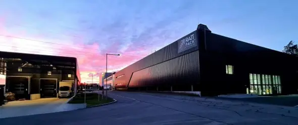 Außenansicht des Rattpack-Werks bei Sonnenuntergang mit modernen Hallen und Zufahrtsstraße.