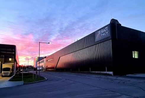 Außenansicht des Rattpack-Werks bei Sonnenuntergang mit modernen Hallen und Zufahrtsstraße.