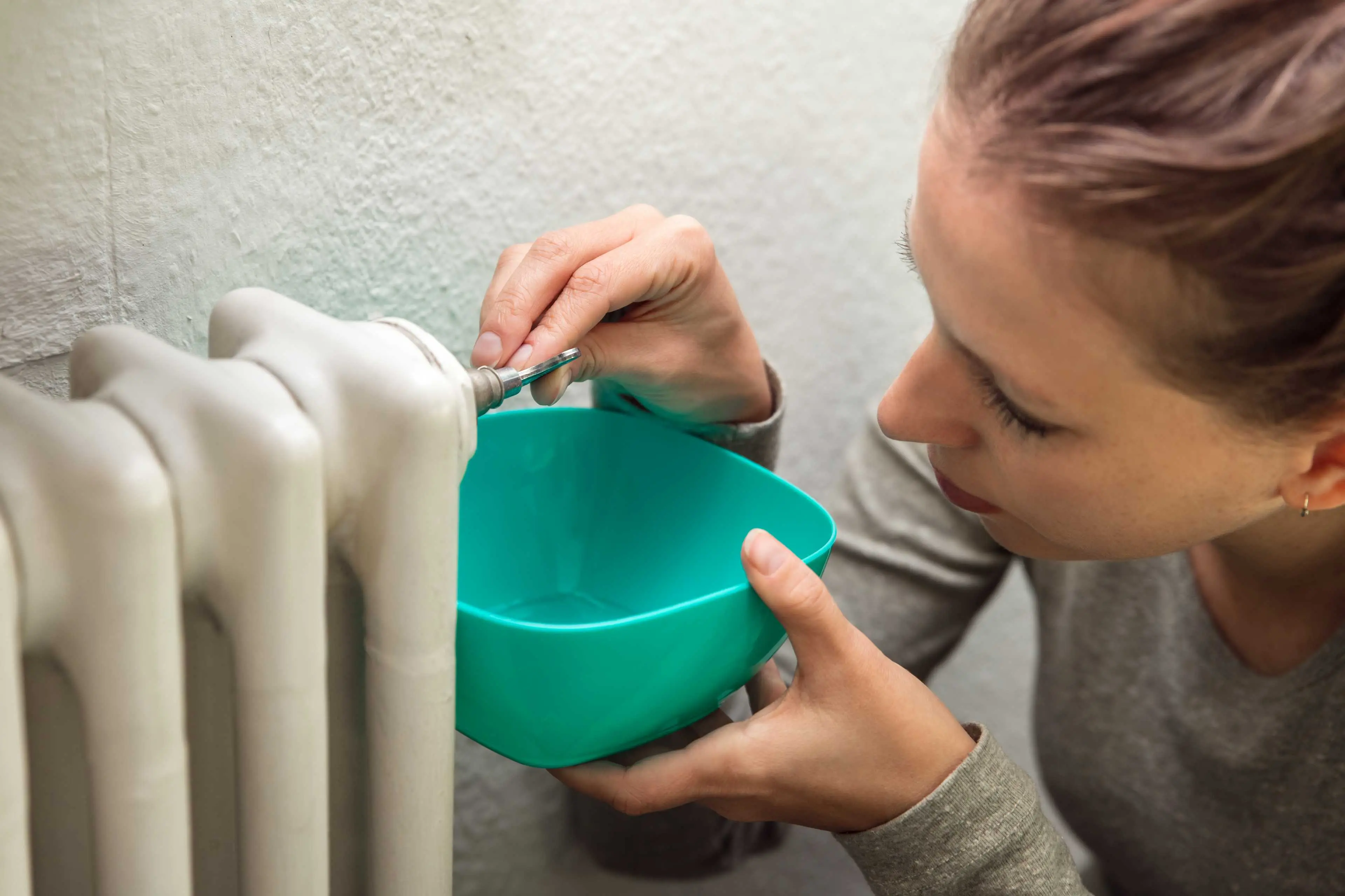 Eine Frau lässt Wasser aus der Heizung ab und fängt es mit einer Plastikschüssel auf