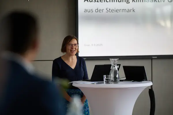 eine Frau spricht zu einer Gruppe, im Hintergrund eine Präsentation