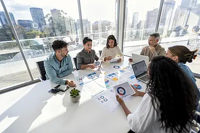 Eine Gruppe sitz im Besprechungsraum und bespricht Auswertungen und Diagramme