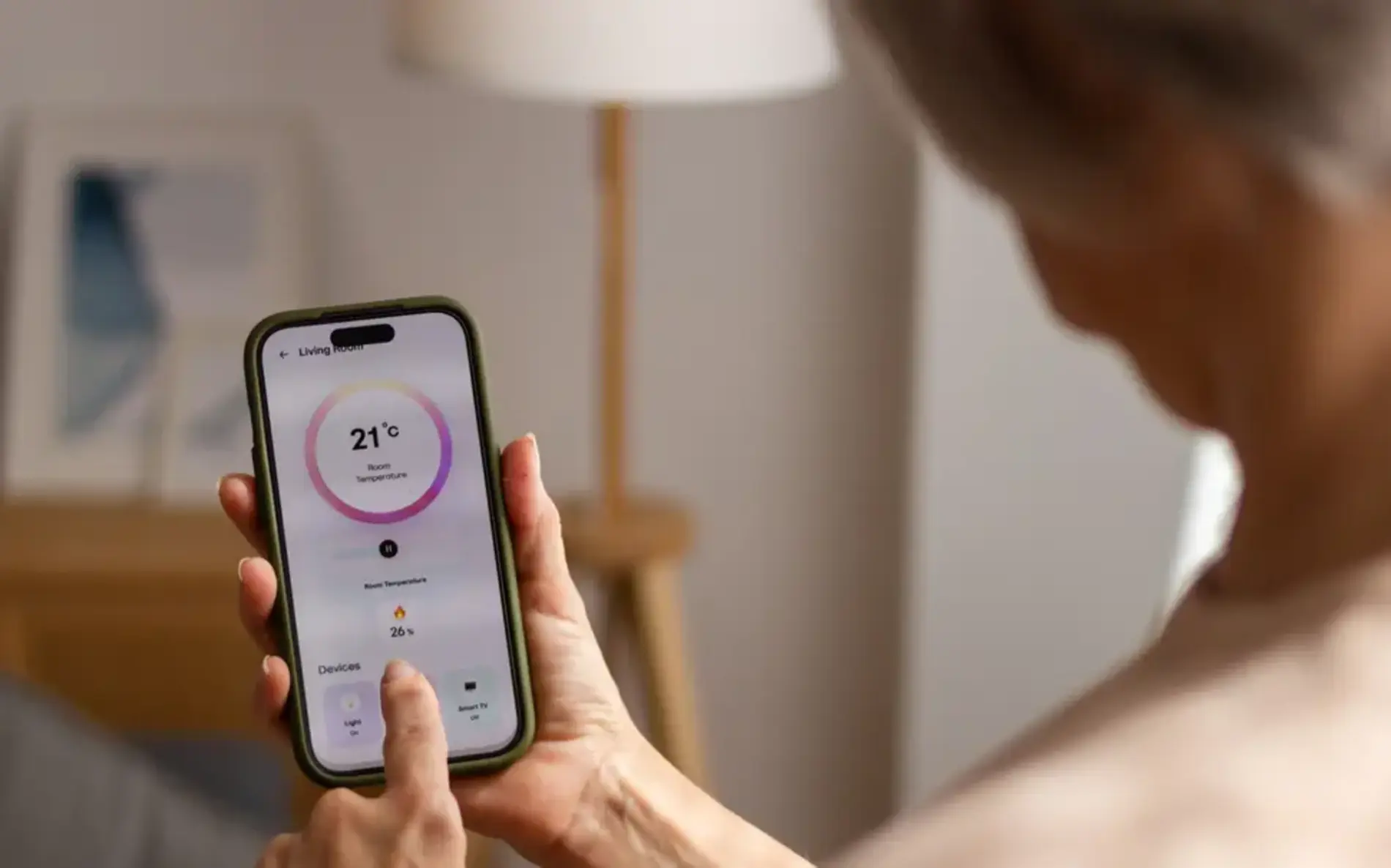 Eine Frau sitzt auf der Couch, sie ist von hinten zu sehen, wie sie auf ihrem Smartphone ihre Heizung steuert