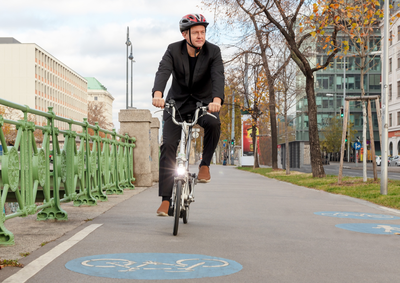 Mann mit Helm, gekleidet mit Sakko, fährt mit Faltrad.