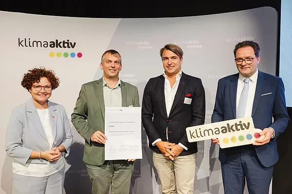 Menschen mit Urkunde und klimaaktiv Schild lächeln in die Kamera
