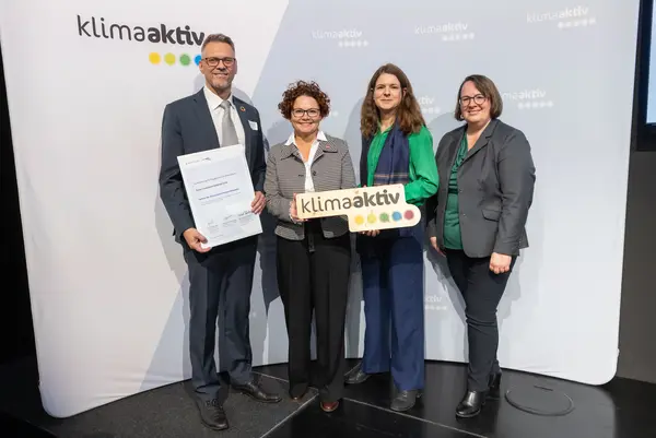 4 Personen mit Urkunde und klimaaktiv Schild schauen in die Kamera