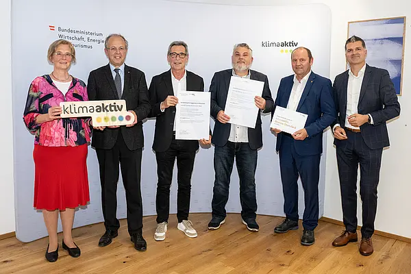 eine Gruppe von Menschen auf einer Bühne hält Urkunden in die Kamera