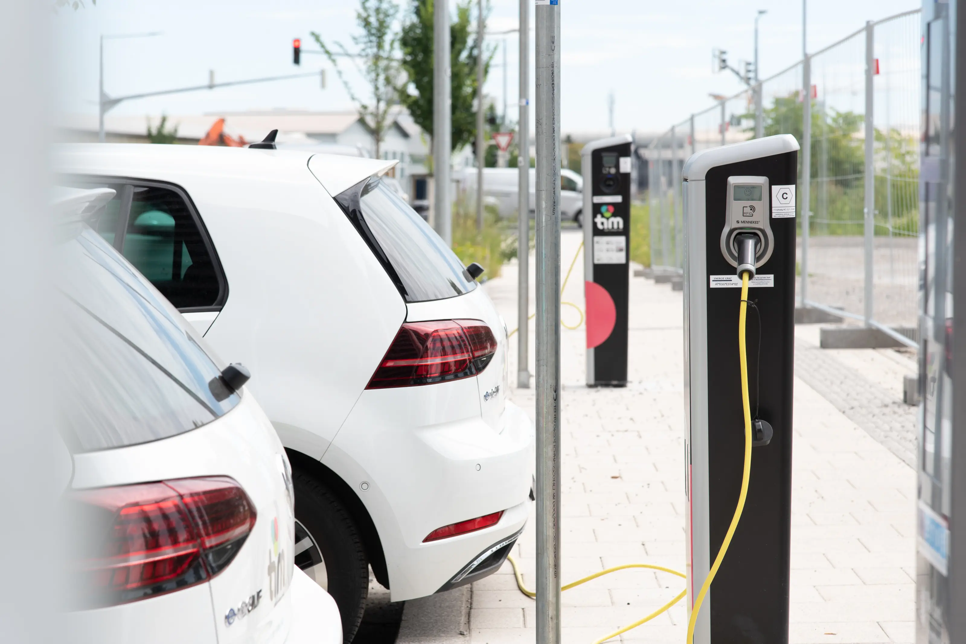 Zwei weiße E-Autos laden gerade mit Kabel an einer Säule auf.
