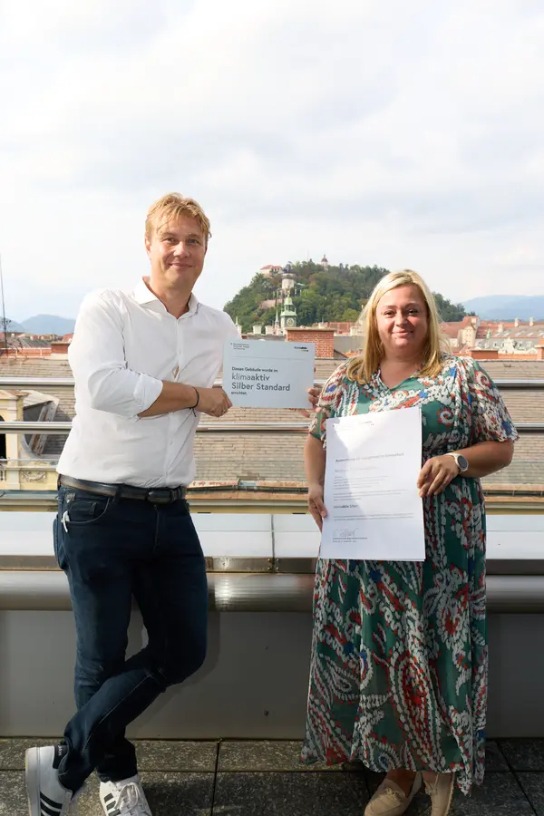 2 Personen mit Urkunde schauen in die Kamera