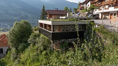 Am Hügel liegt ein verwilderter Garten, daneben steht ein haus