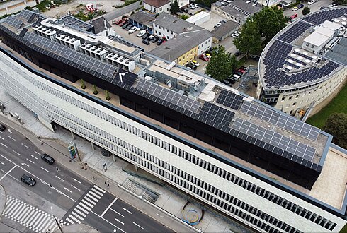 Luftbild eines langen Gebäudes mit Solarpaneelen auf dem Dach, angrenzend an eine Straße.