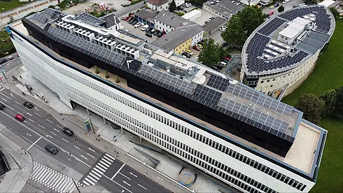 Luftbild eines langen Gebäudes mit Solarpaneelen auf dem Dach, angrenzend an eine Straße.