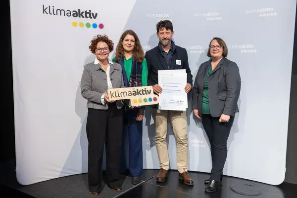 4 Personen mit Urkunde und klimaaktiv Schild schauen in die Kamera