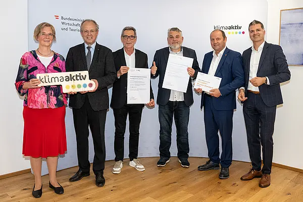 eine Gruppe von Menschen auf einer Bühne hält Urkunden in die Kamera