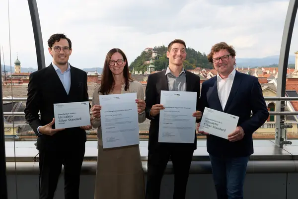 4 Personen mit Urkunden schauen in die Kamera