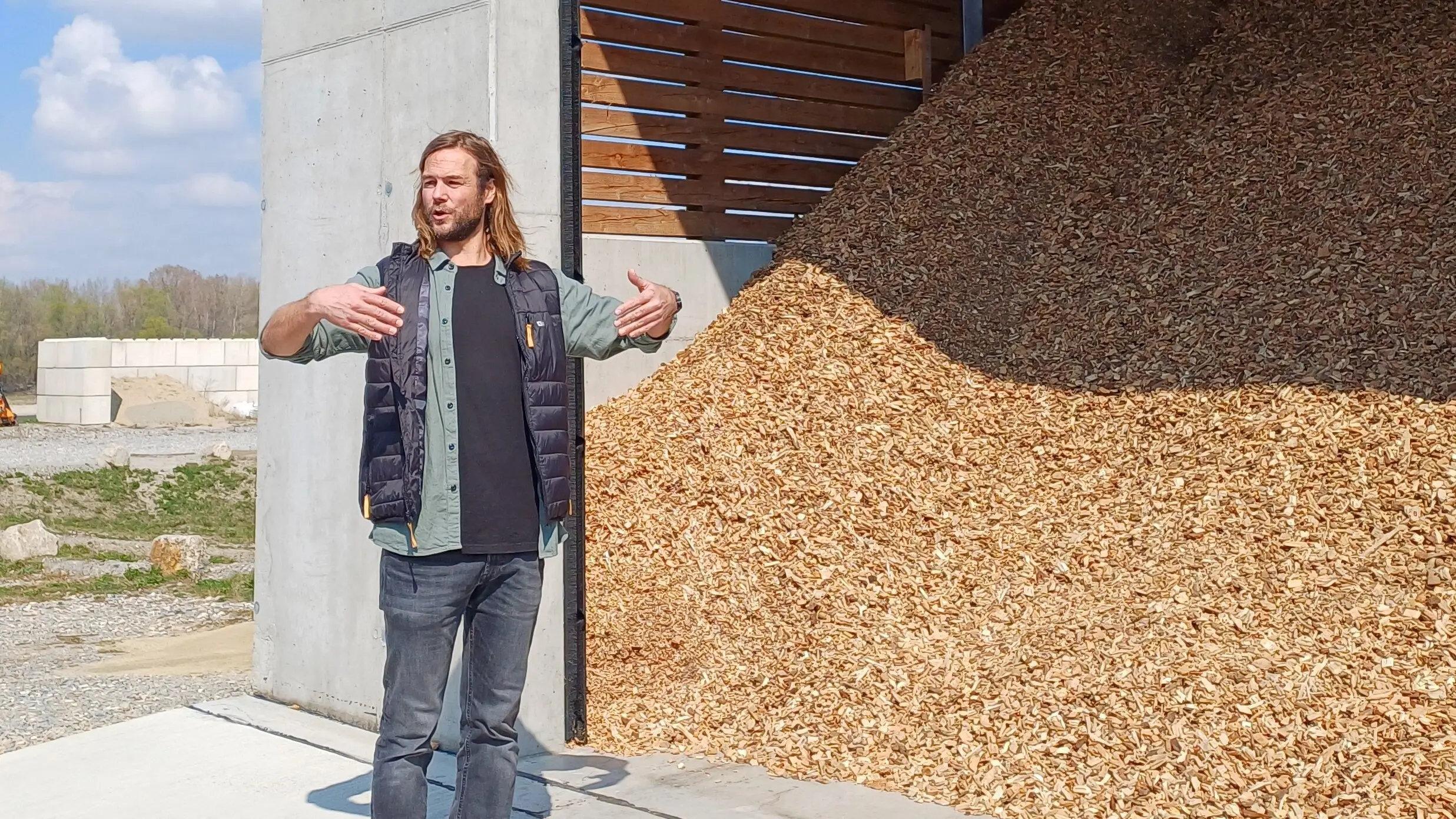 Person steht vor einem großen offenen Lagerbereich, der mit Holzschnitzeln gefüllt ist, und gestikuliert mit den Händen.