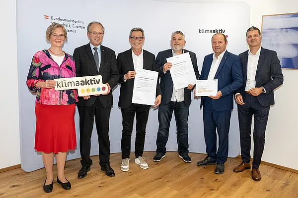 eine Gruppe von Menschen auf einer Bühne hält Urkunden in die Kamera