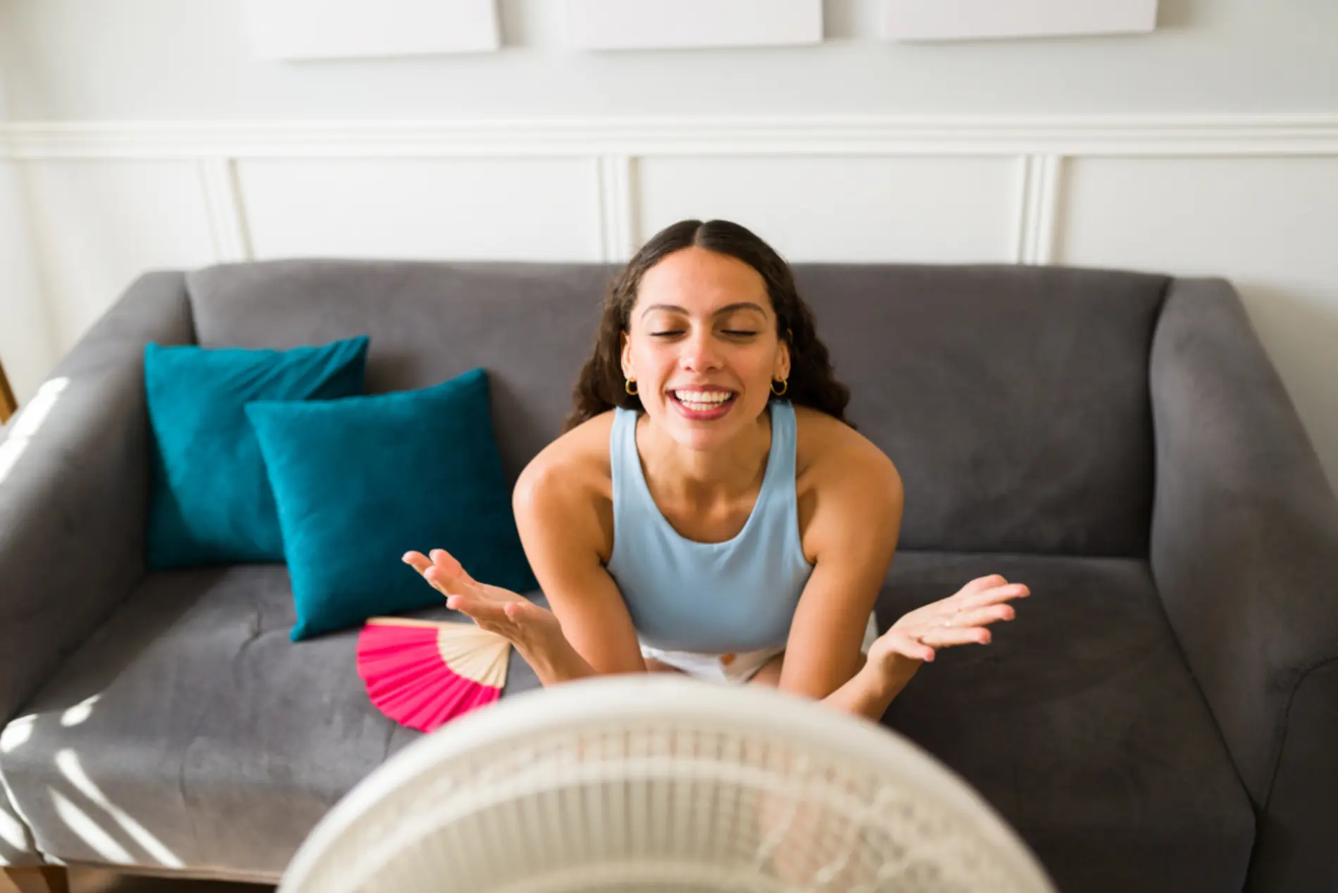 Eine Frau sitzt auf einem Sofa vor einem Ventilator und genießt dabei die kühle Luft. 