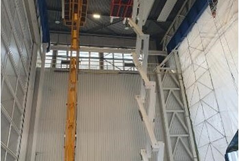 Innenansicht einer hohen Industriehalle mit Hebebühnen und Montagearbeiten an der Decke.