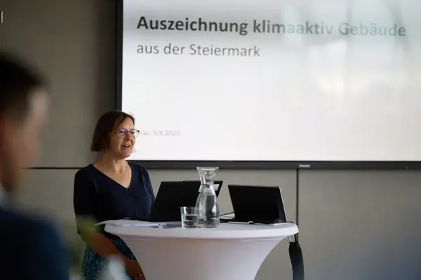 eine Frau spricht zu einer Gruppe, im Hintergrund eine Präsentation