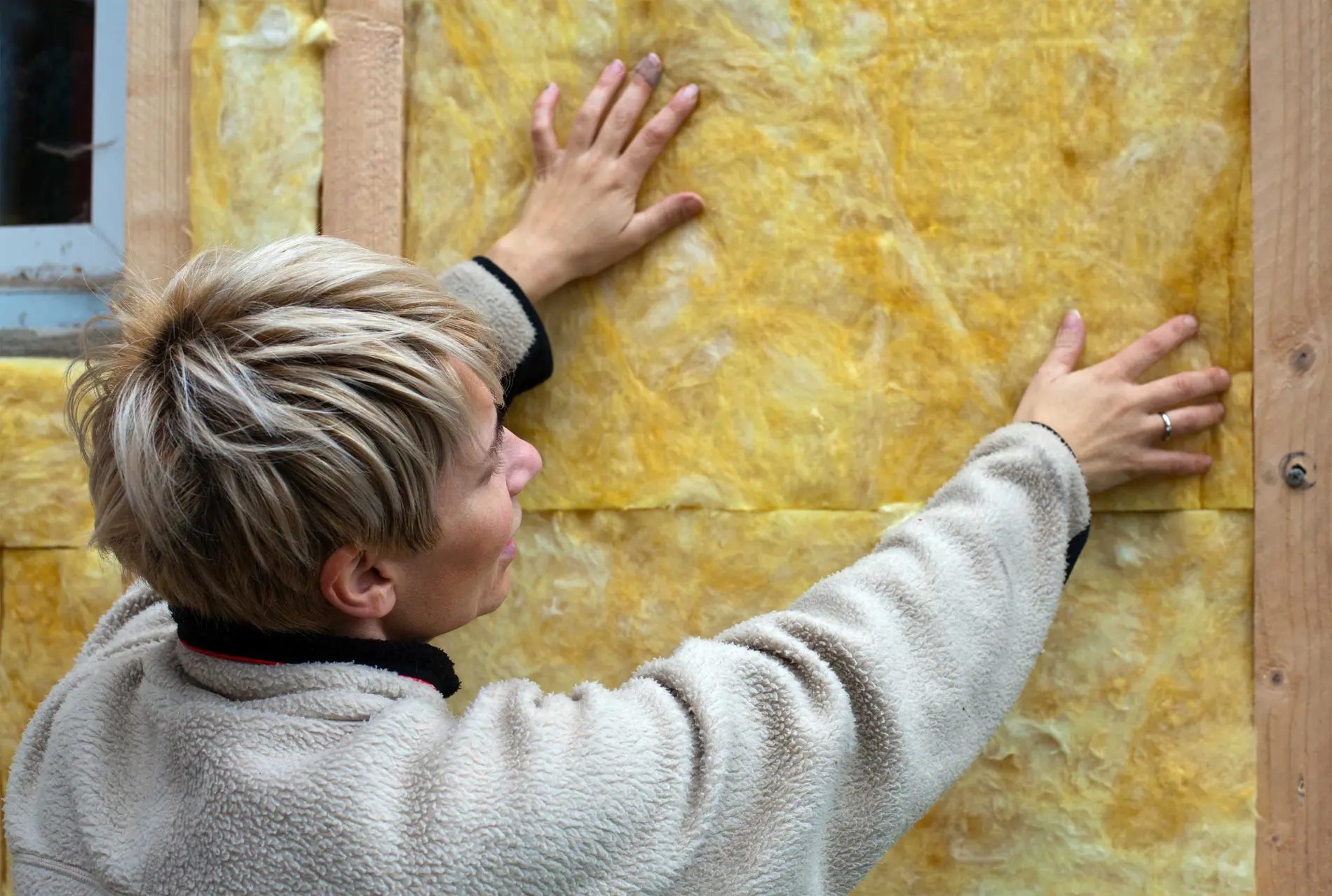 Frau hält betastet Dämmstoff am Haus.