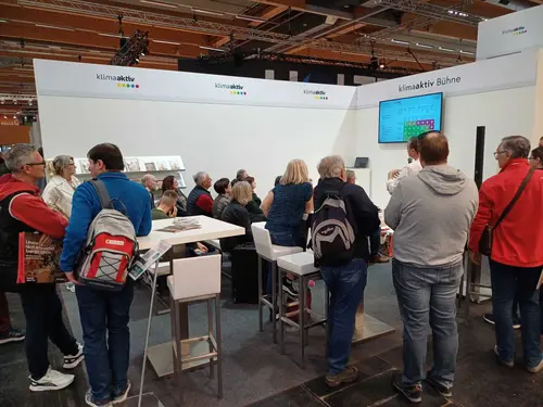 mehrere Menschen stehen vor einer kleinen Bühne und hören zu