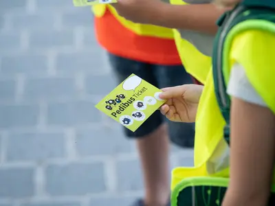 Kinderhand hält ein Pedibus-Ticket
