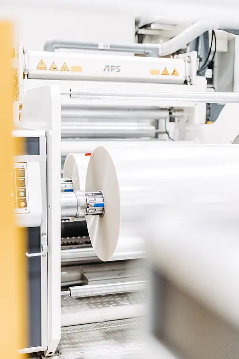 Industriemaschine mit großen Rollen für Folienverarbeitung in einer Produktionshalle.