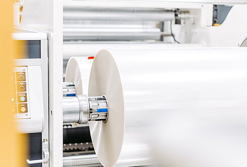 Industriemaschine mit großen Rollen für Folienverarbeitung in einer Produktionshalle.