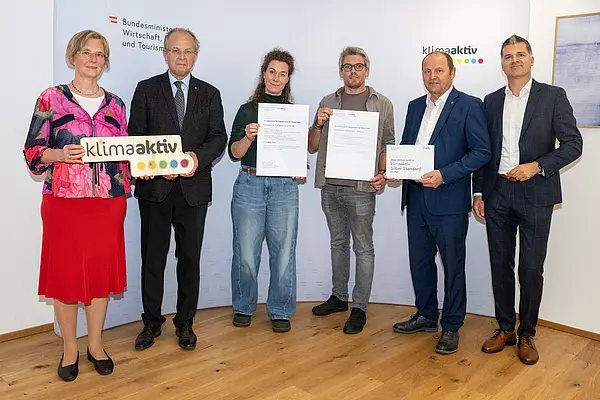 eine Gruppe von Menschen auf einer Bühne hält Urkunden in die Kamera