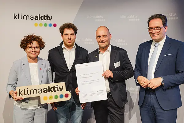 Menschen mit Urkunde und klimaaktiv Schild lächeln in die Kamera