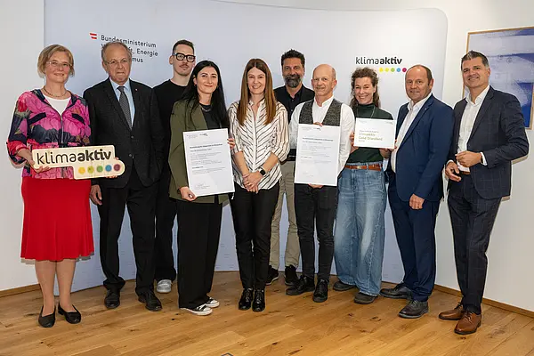 eine Gruppe von Menschen auf einer Bühne hält Urkunden in die Kamera