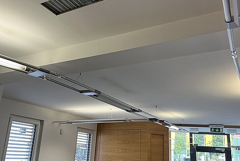 Innenansicht eines modernen Büros mit Schreibtischen, Monitoren und großen Fenstern. Lüftungsschlitz an der Decke