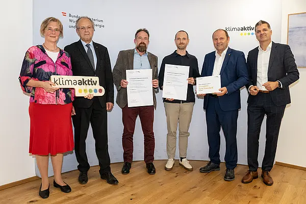eine Gruppe von Menschen auf einer Bühne hält Urkunden in die Kamera
